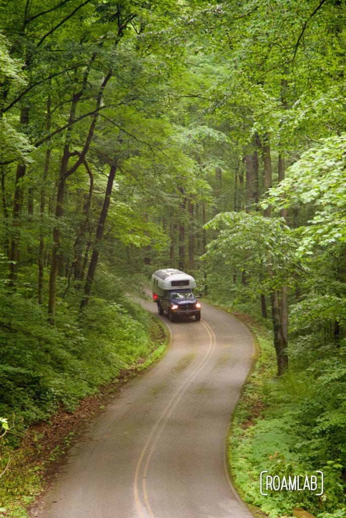 1970 Avion C11 truck camper driving down the winding paved two-lane Houchin Ferry Road in Mammoth Cave National Park.