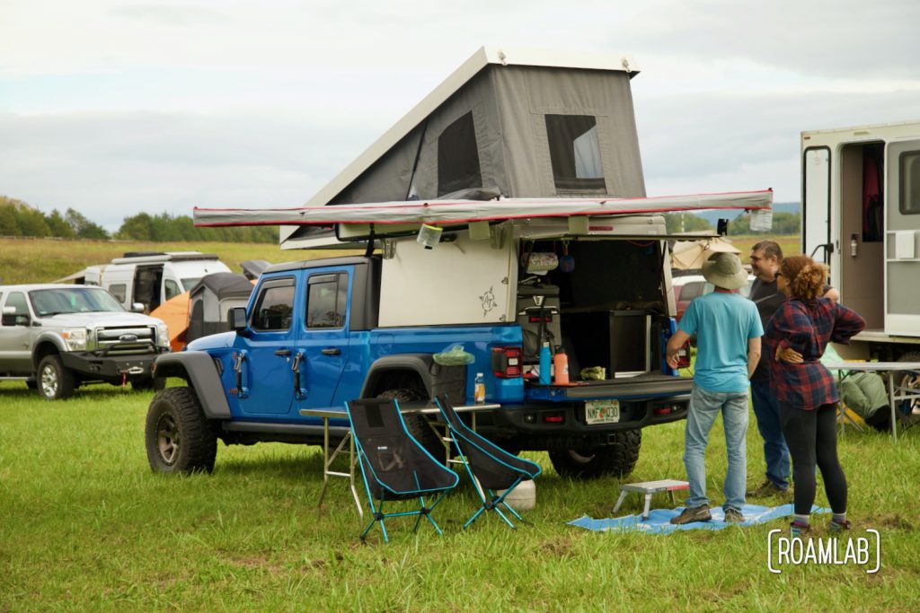 A trio of attendees exploring a popup camper on an electric blue Jeep at Overland Expo East 2021 in Arrington, Virginia.