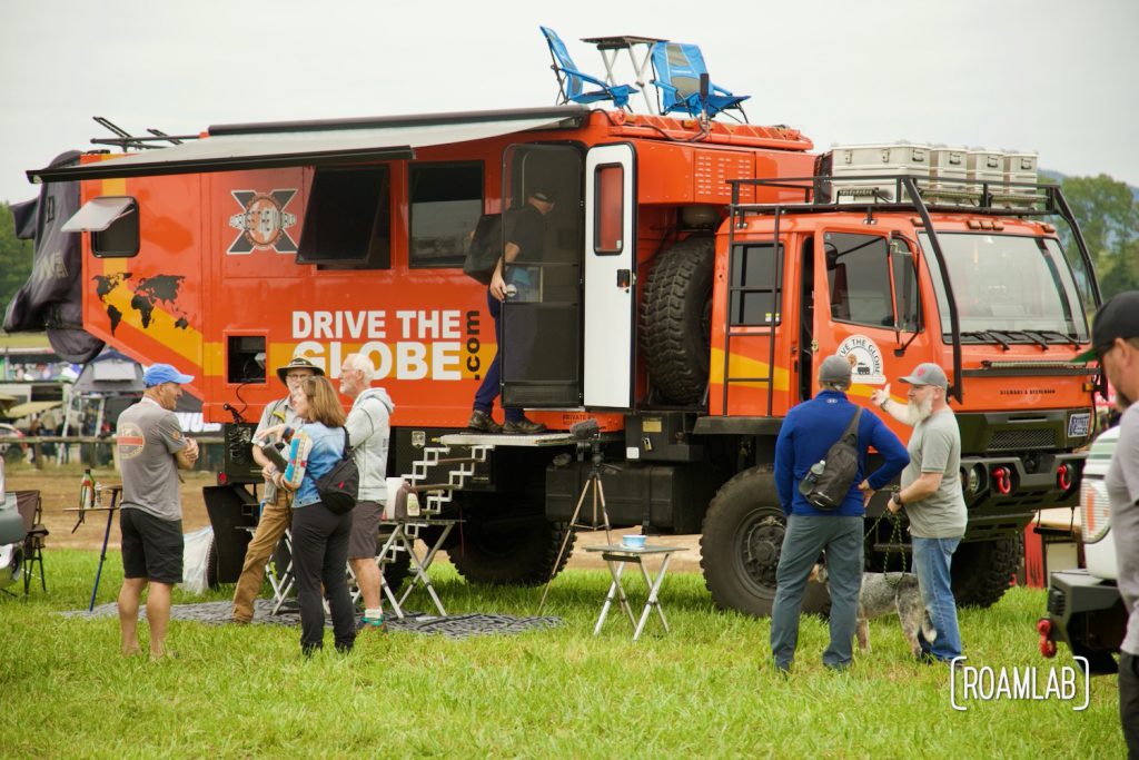 Crowd of attendees exploring and discussing a massive orange overland rig at Overland Expo East 2021 in Arrington, Virginia.