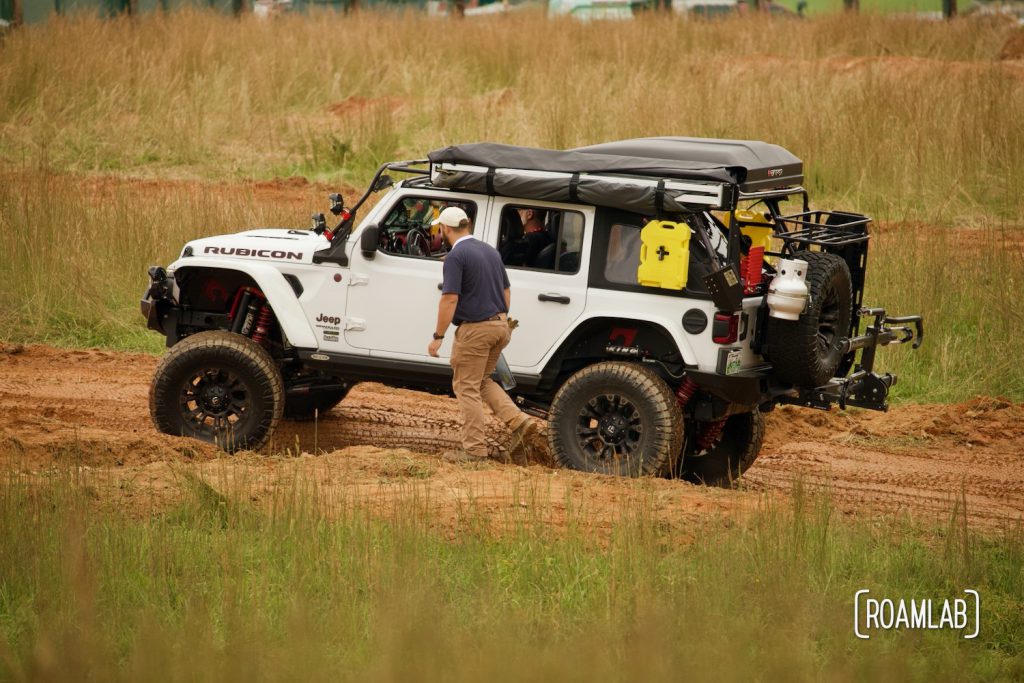 Man walking along a white Jeep along an uneven dirt course at Overland Expo East 2021 in Arrington, Virginia.