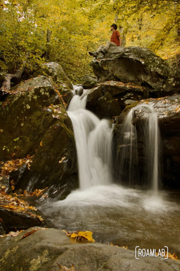 Man sitting on a rock over a small waterfall along Dark Hollow Falls in Shenandoah National Park.