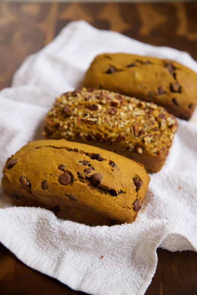 Three loaves of pumpkin bread sitting on a hand kitchen towel.