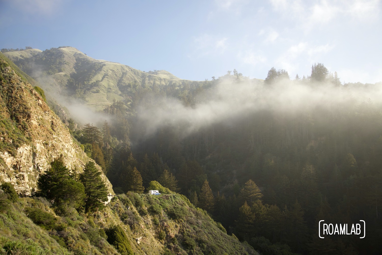 Morning mist lingering over the mountains of Big Sur, California with a 1970 Avion C11 truck camper in the distance.