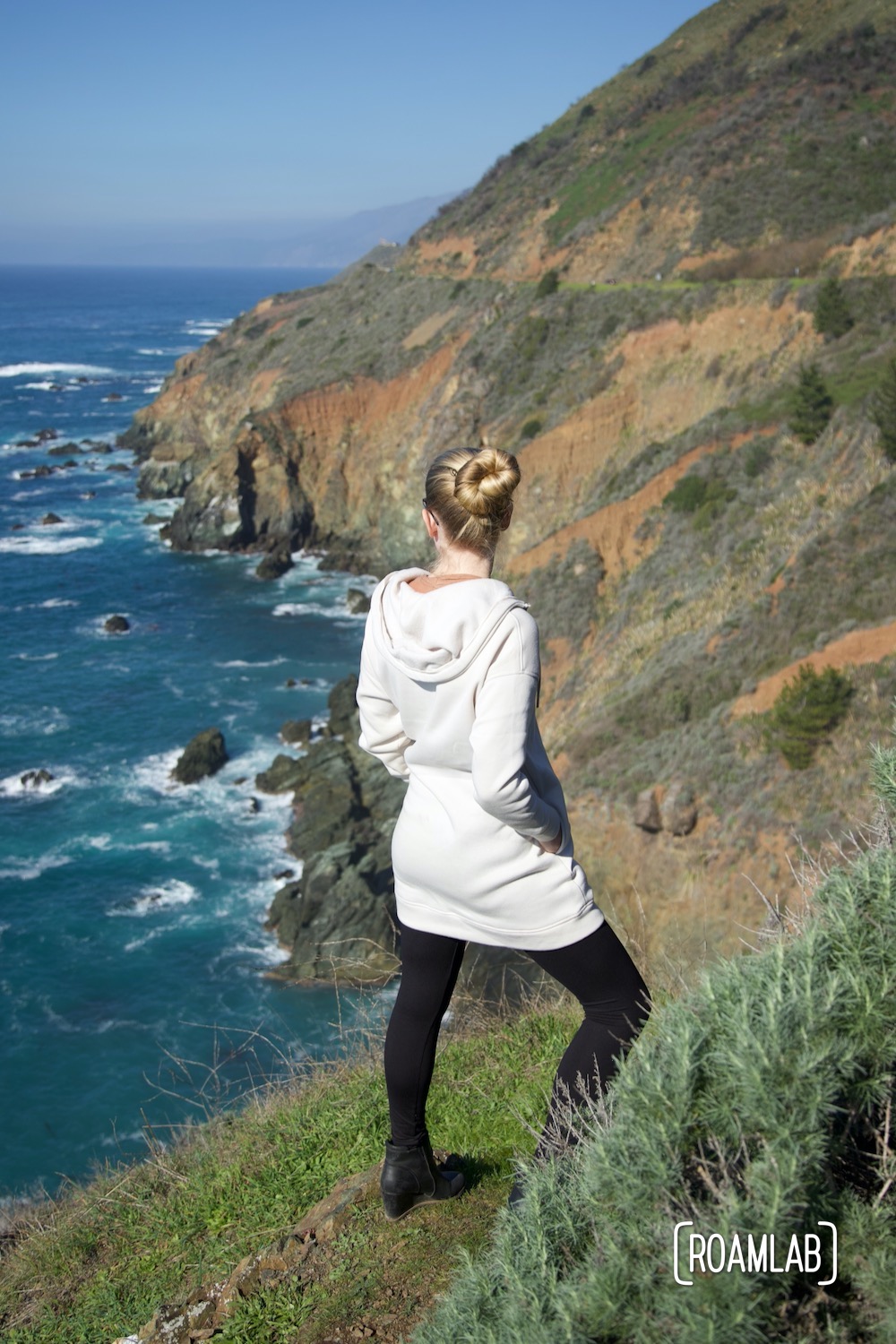 Woman standing along a cliffside, looking out over the Pacific Ocean in Big Sur, California.