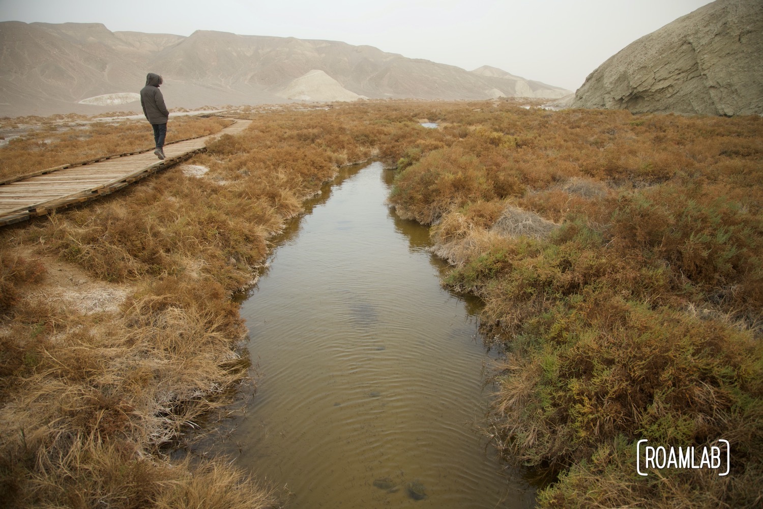 Man on a boardwalk running parallel to a creek.