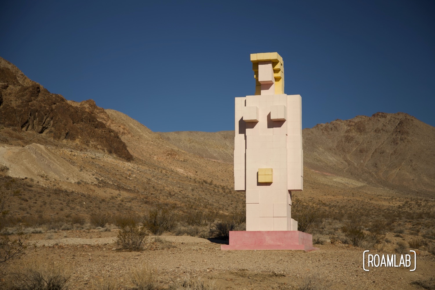 Pixilated sculpture of nude Venus kneeling in the desert.