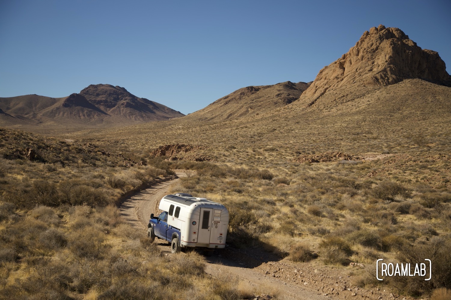 Mountains rising in the distance as a 1970 Avion C11 truck camper following the winding desert dirt Titus Canyon Road in Death Valley National Park, California.