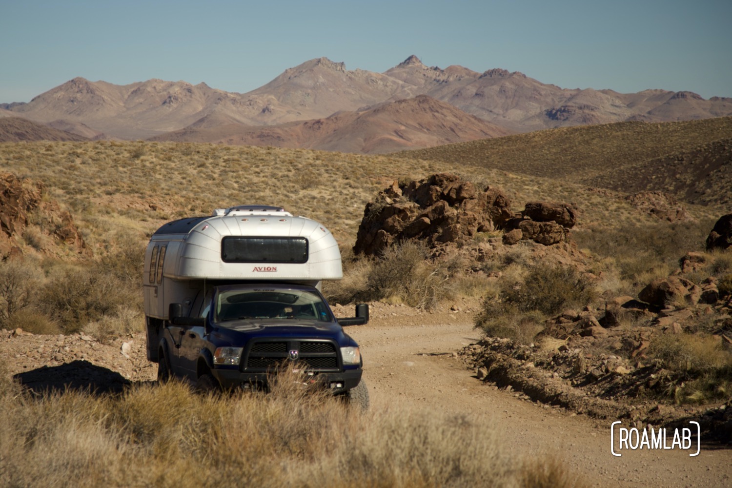 A view of Nevada's mountains in the background of a 1970 Avion C11 truck camper following the dirt Titus Canyon Road in Death Valley National Park, California.