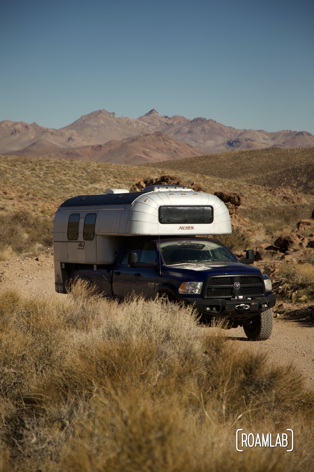 Nevada mountains rising in the distance behind a 1970 Avion C11 truck camper following the dirt Titus Canyon Road in Death Valley National Park, California.