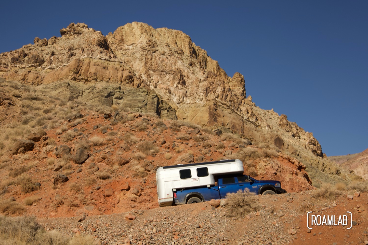 Colorful red cliffs of the Red Pass as a 1970 Avion C11 truck camper following the dirt Titus Canyon Road in Death Valley National Park, California.