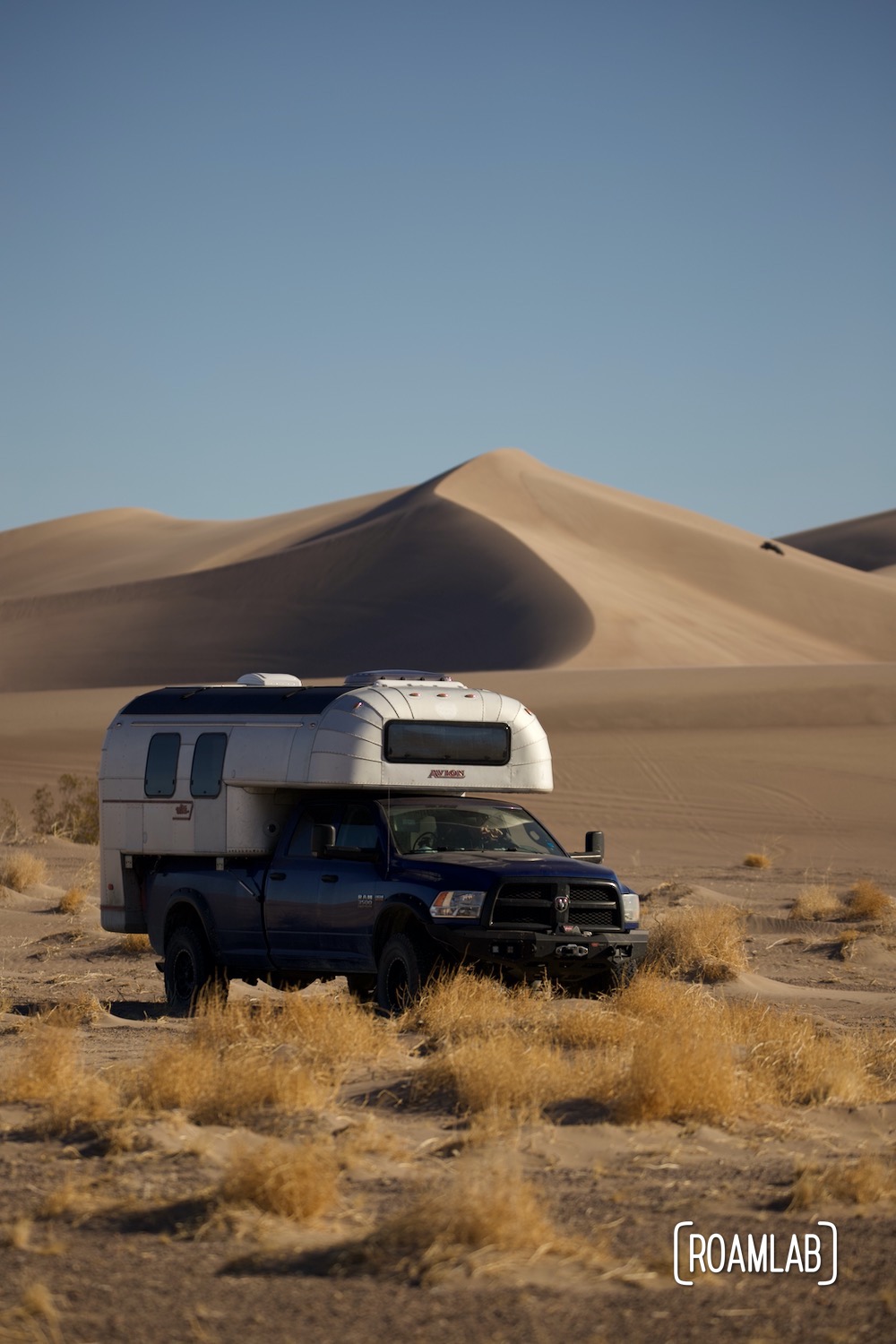 1970 Avion C11 truck camper parked in the sand in front of the dunes of Big Dune Recreational Area.