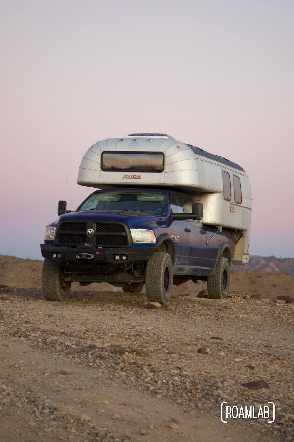 1970 Avion C11 truck camper parked on a dirt ridge with the sunset in the background.