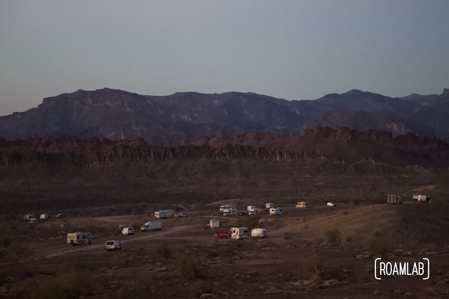 Campers scattered across the valley floor with mountains in the distance at dusk.