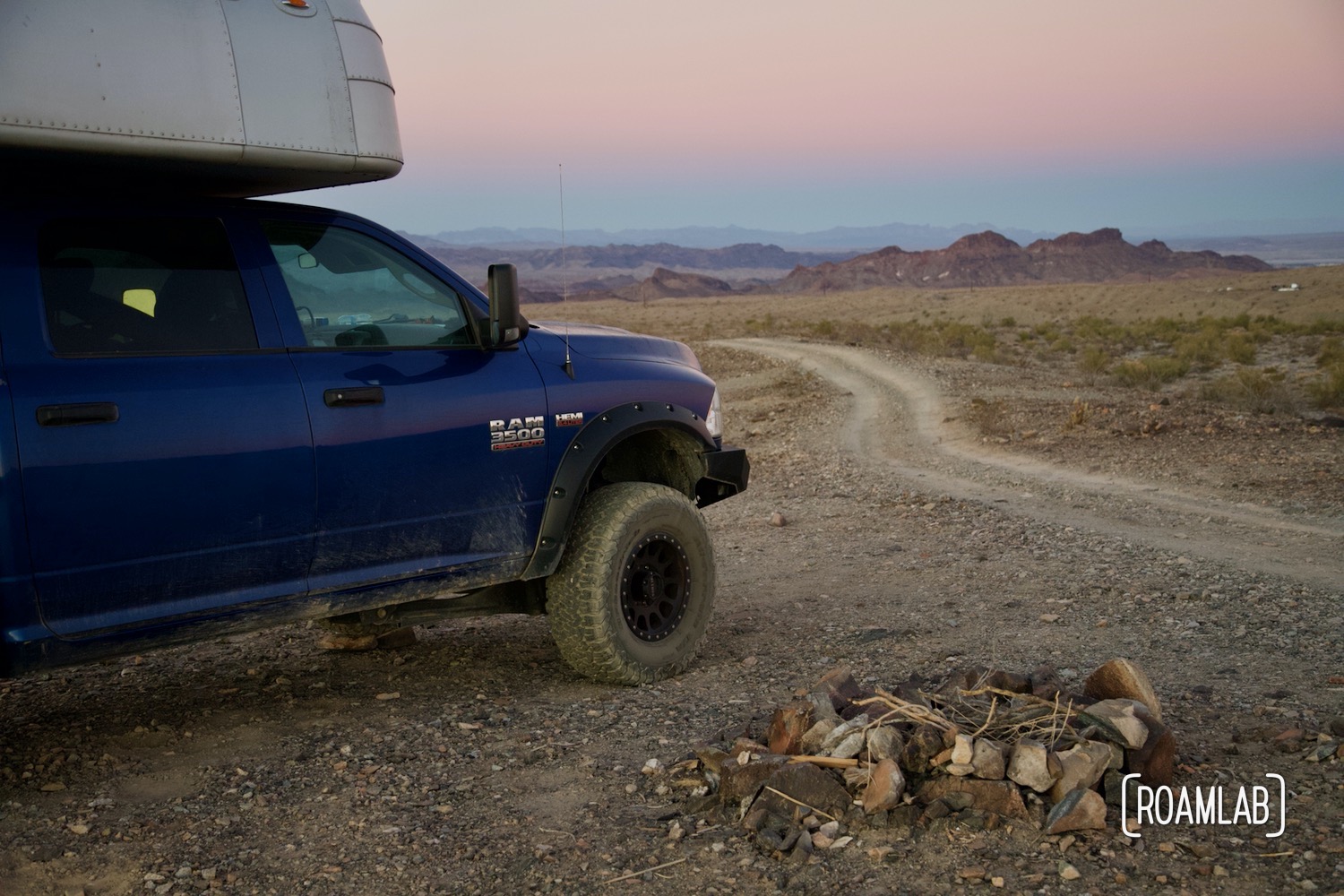 Truck and camper parked by a fire ring at sunset.