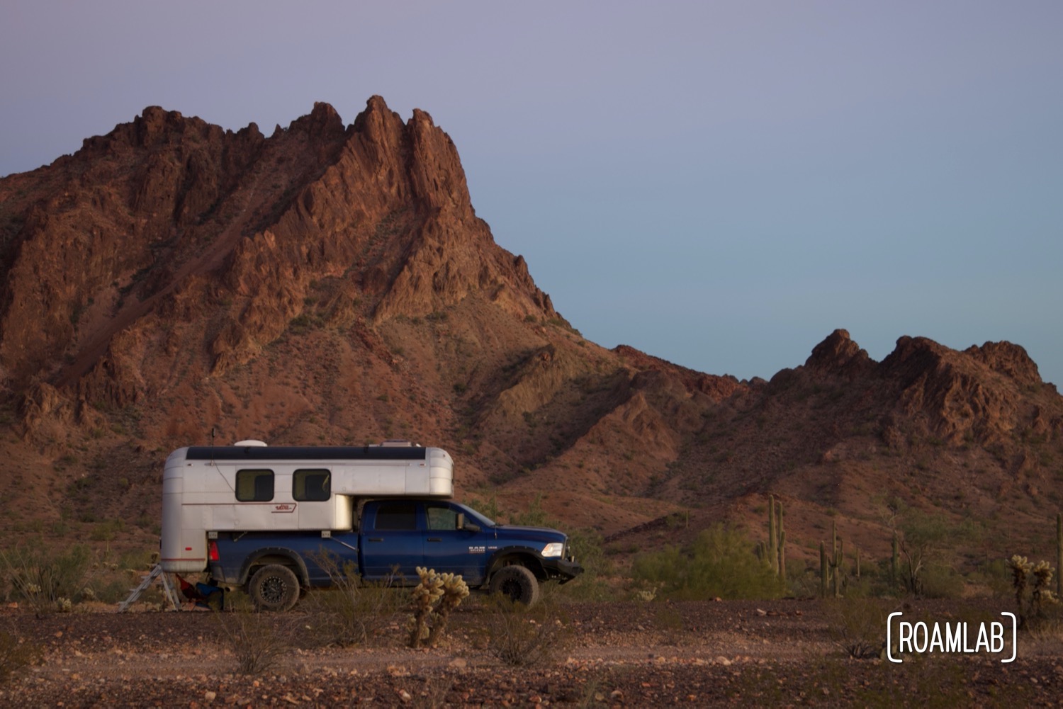 1970 Avion C11 truck camper parked in front of a dramatic desert mountain range in Kofa Wilderness Refuge.