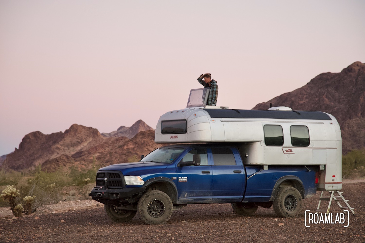 Man popping out of the roof hatch of a 1970 Avion C11 truck camper at dawn in Kofa Wilderness Refuge.