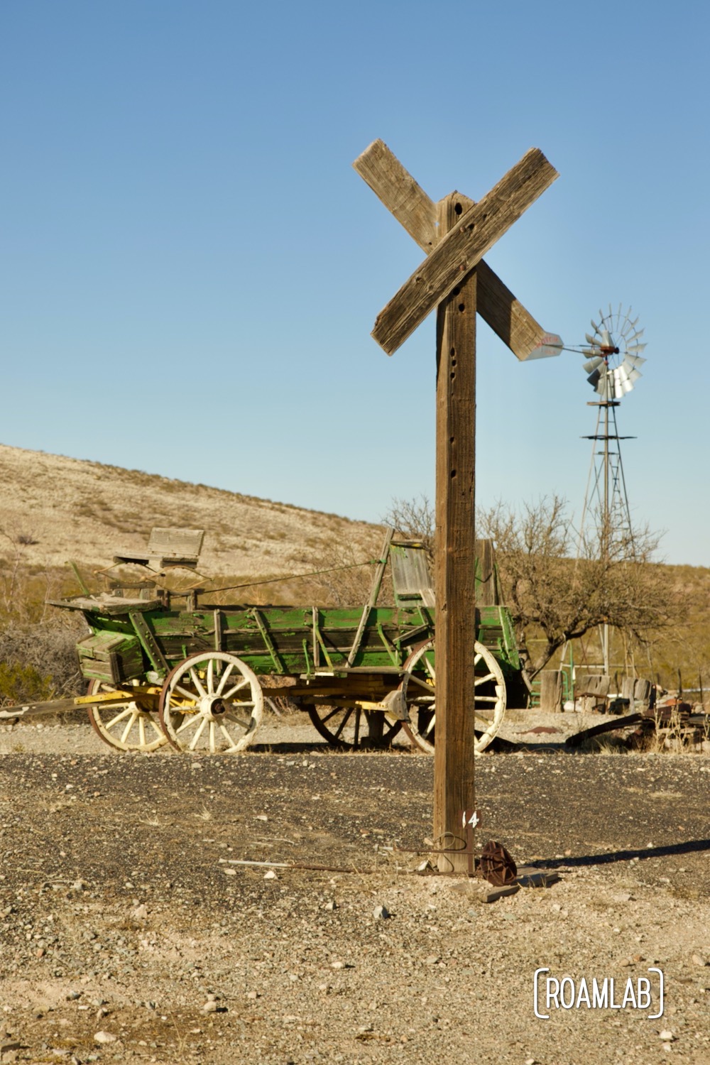 Green wagon in front of a wood structure with a windmill in the background in Shakespeare Ghost Town, New Mexico.