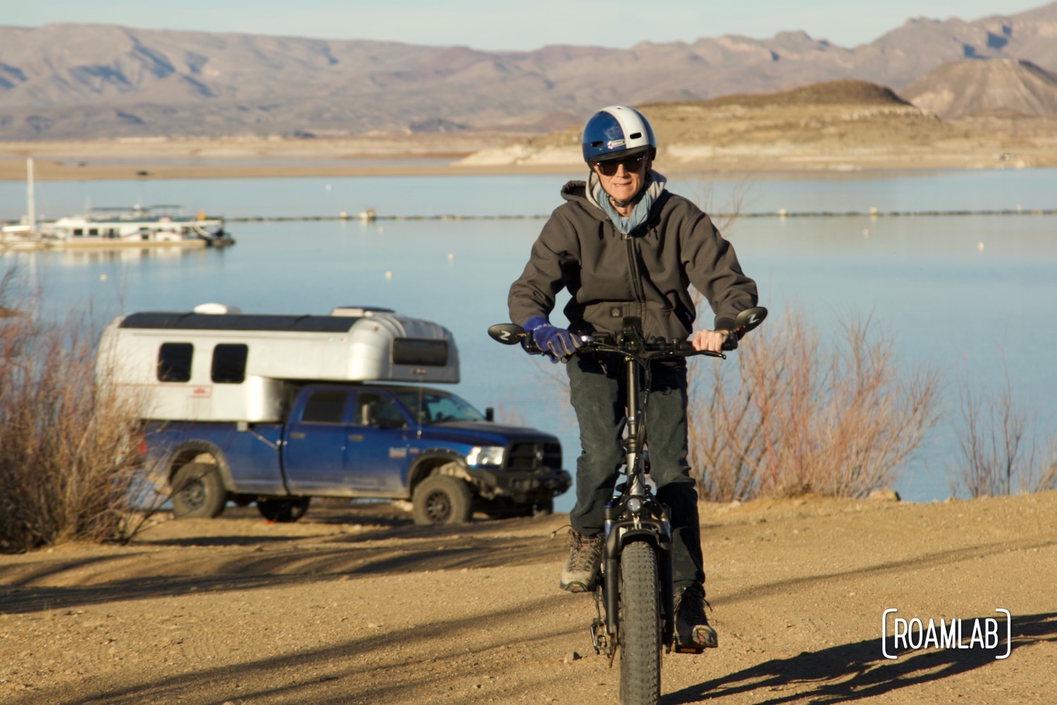 Man riding a bike in front of a 1970 Avion C11 truck camper and Elephant Butte Lake.