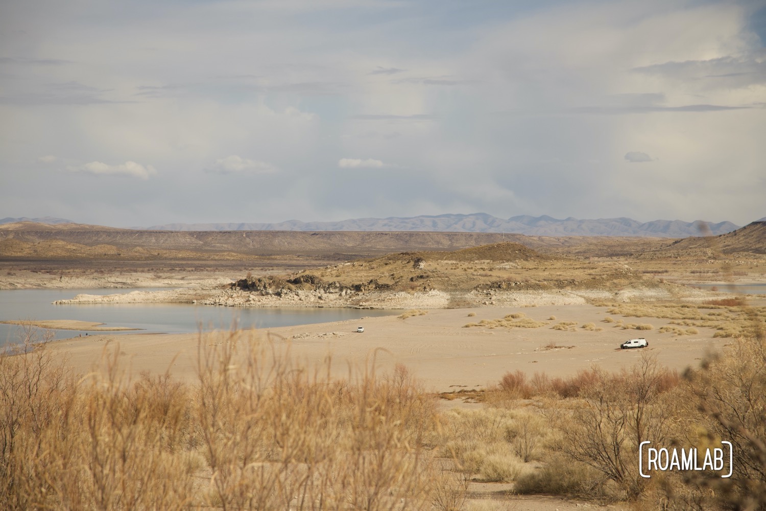 Distant view of Elephant Butte Lake with occasional vehicles parked along the shore.