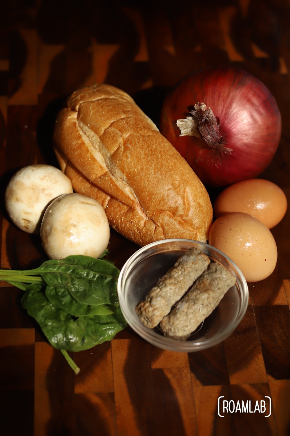 Key ingredients for our egg boats dutch oven campfire cooking recipe laid out (hoagie roll, red onion, white mushrooms, eggs, sausage, spinach)