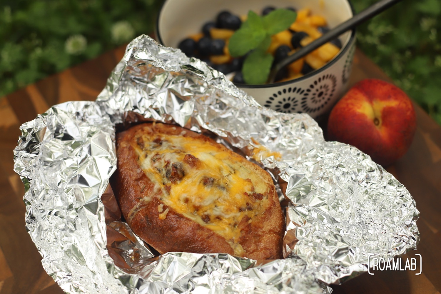 Egg boat wrapped in tin foil with a bowl of peaches and blueberries topped with a sprig of mint.