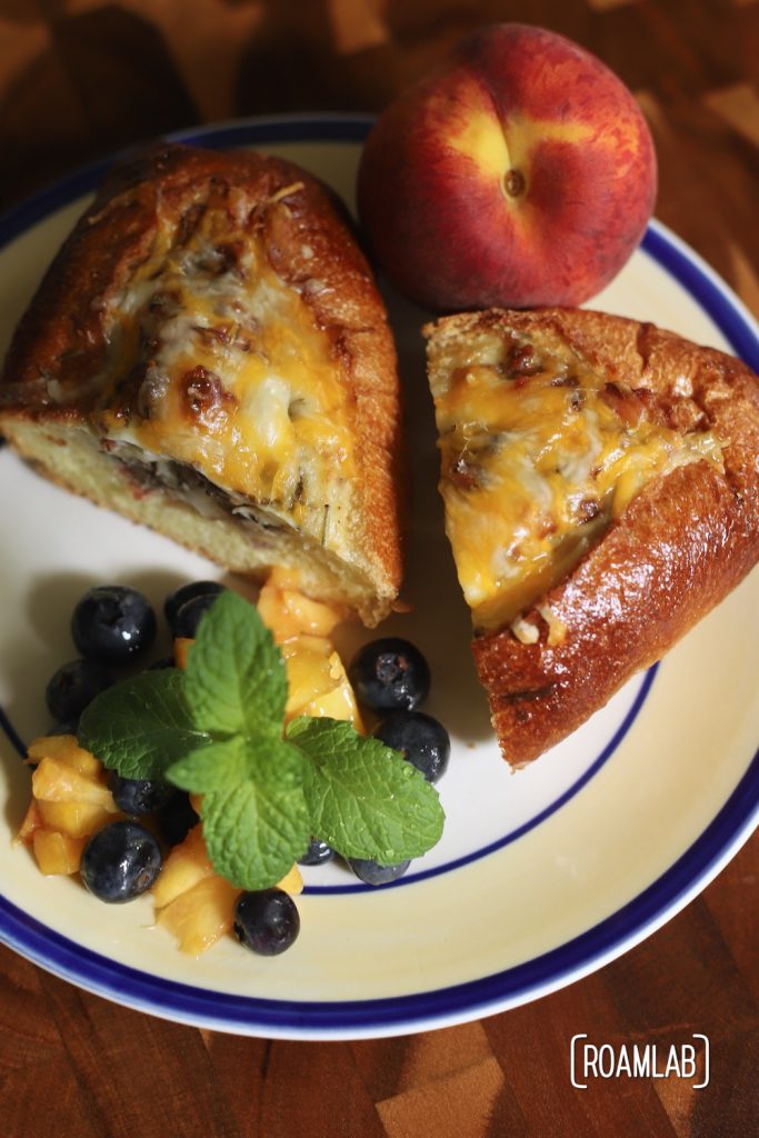 Egg boat cut in half on a plate with peach and blueberry fruit salad topped with a sprig of mint.