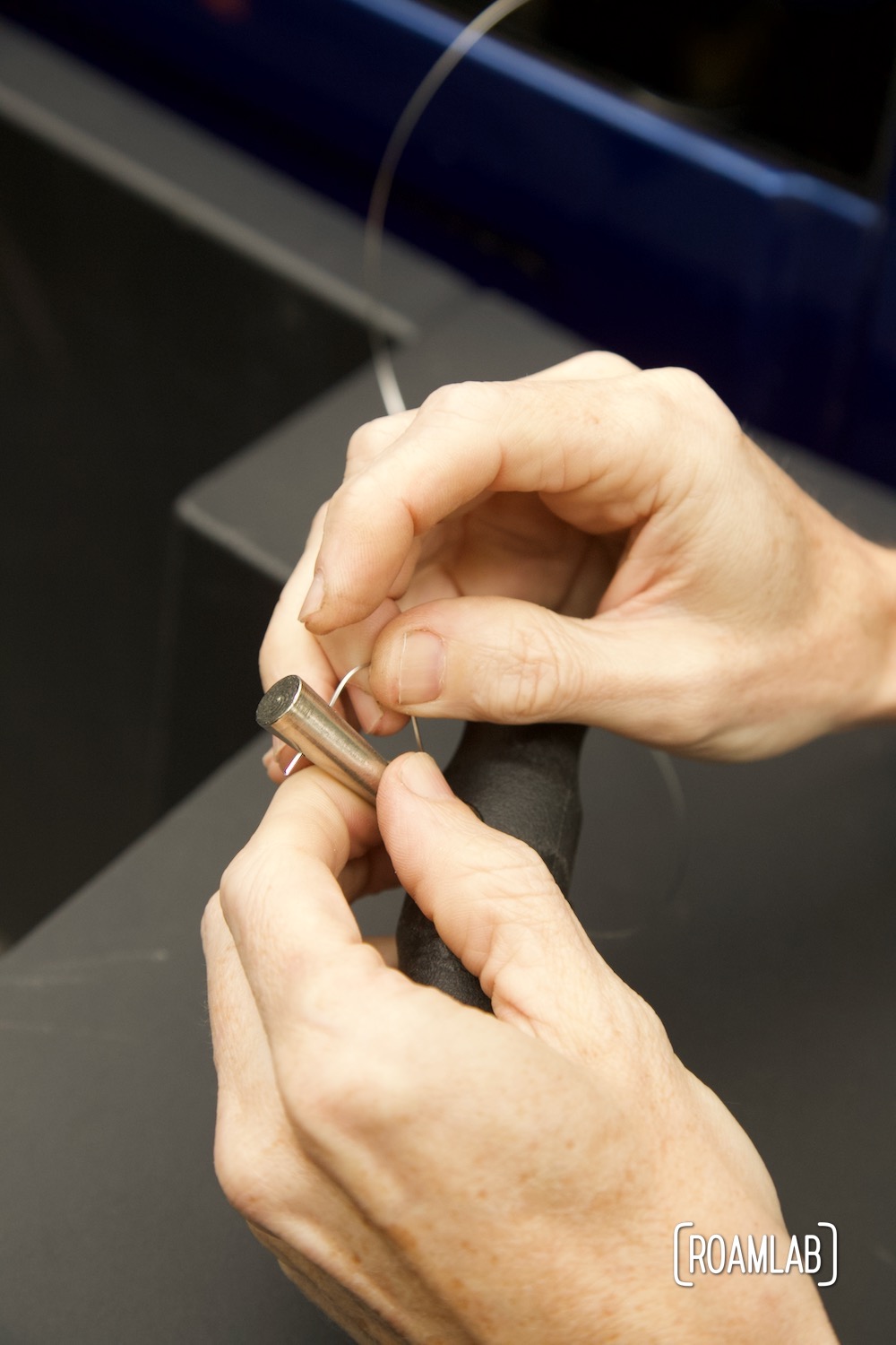 Hands pushing the cutting wire end through the tip of the gripping handle shaft to secure it in place.