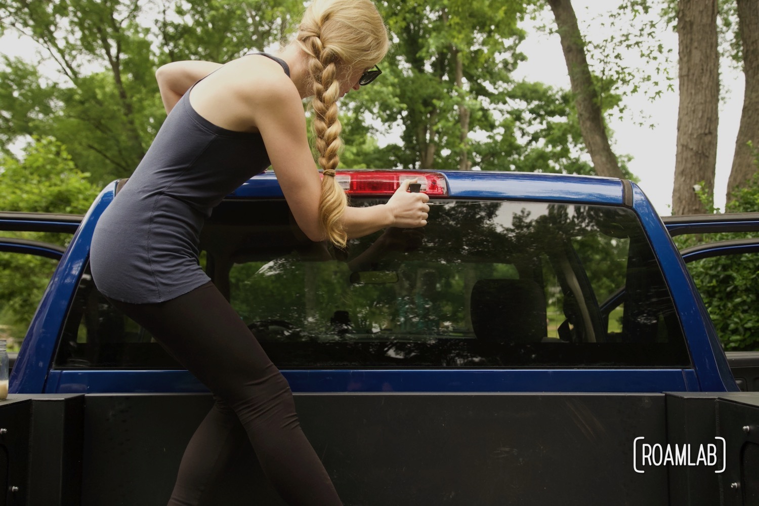 Woman pulling a cutting wire with gripping handles along the top edge of a truck cabs rear windshield.