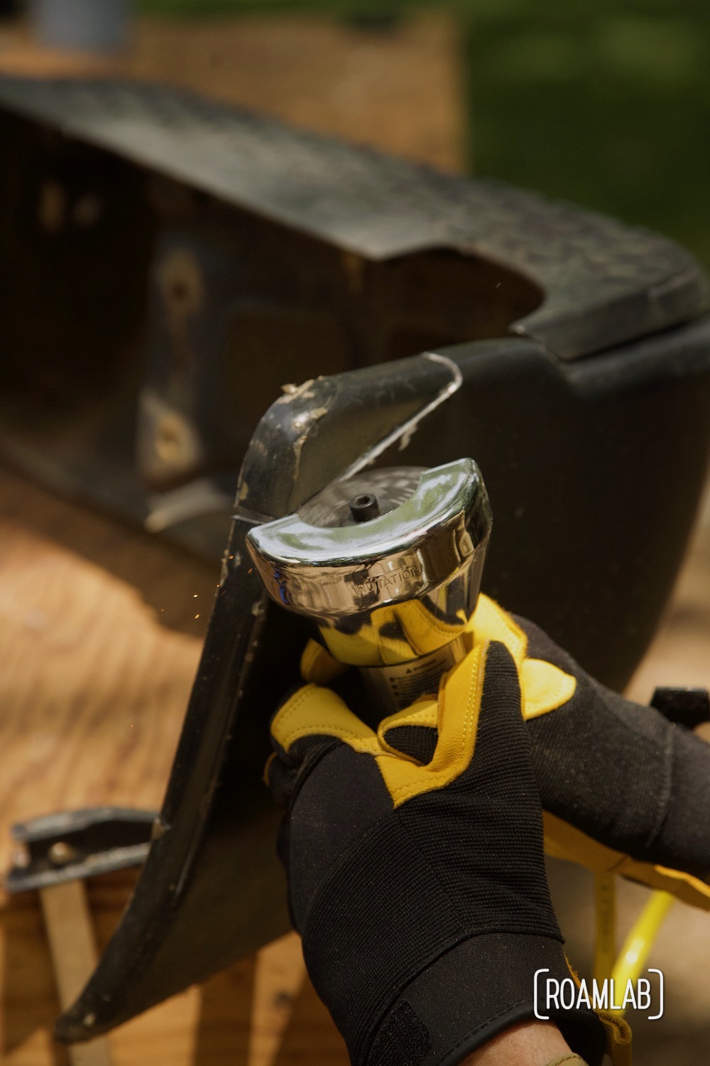 Close up of gloved hands using a cut-off tool to trim a truck bumper.