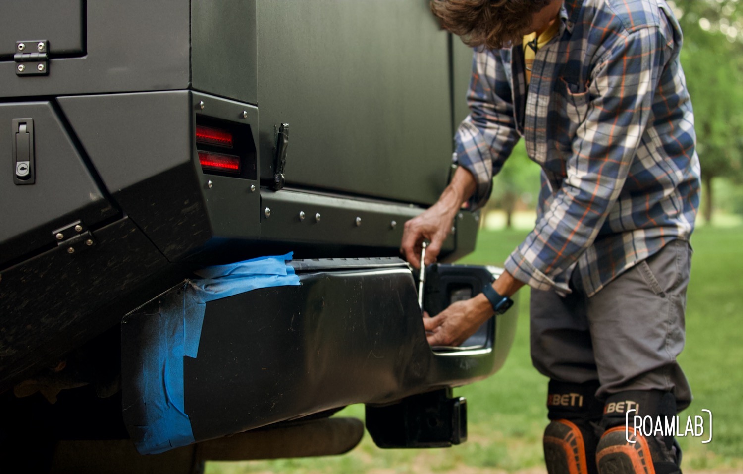 Man using a wrench to bolt a black bumper to a black truck bed.