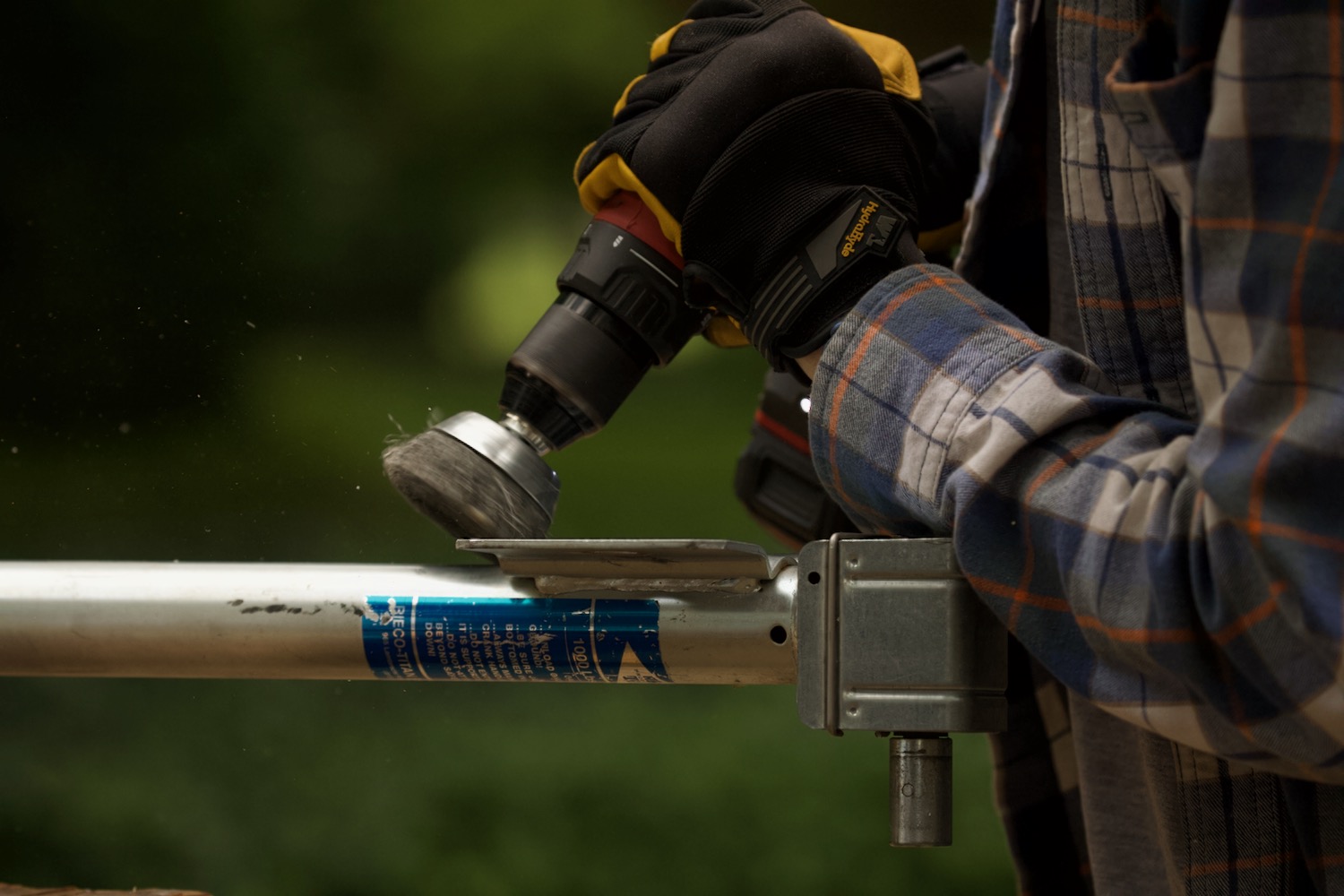 Gloved hands holding a power drill with a metal brush attachment to grind off corrosion on a steel jack.