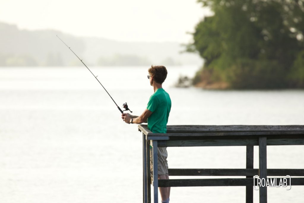 Man fishing on a pier at dusk.