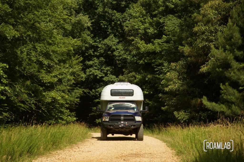 Avion C11 truck camper driving along a graded gravel forest road through dense forest.