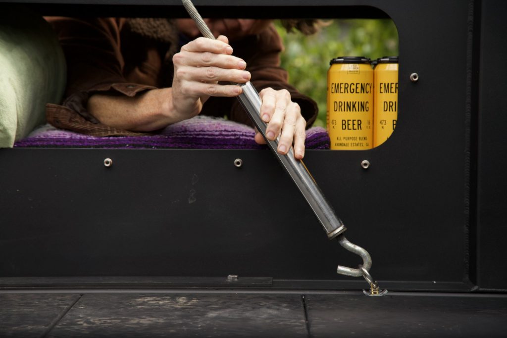 Man adjusting a turnbuckle connecting a truck camper to a custom truck bed.