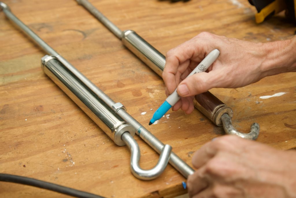 Close up of hands marking a threaded metal rod with a blue permanent marker.