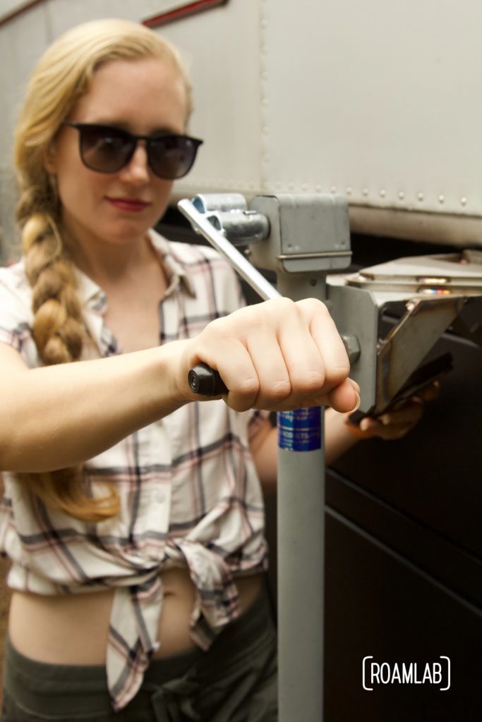 Woman turning a handle to lift a truck camper using jacks.