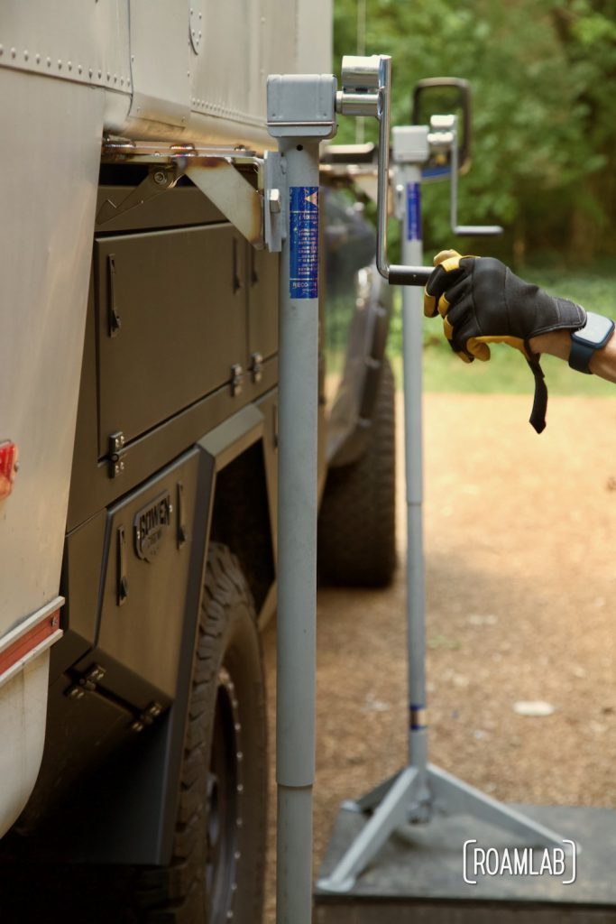 Gloved hand cranking the jack handle to lift the camper out of the truck bed.