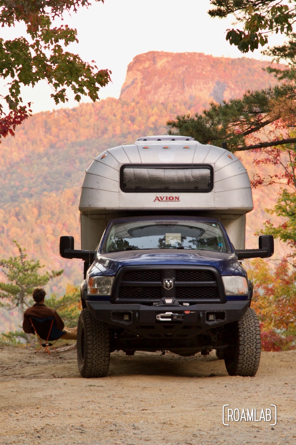 Man sitting next to a 1970 Avion C11 truck camper, taking in a view of Table Rock Mountain from Old North Carolina 105 in Linville Gorge Wilderness Area.