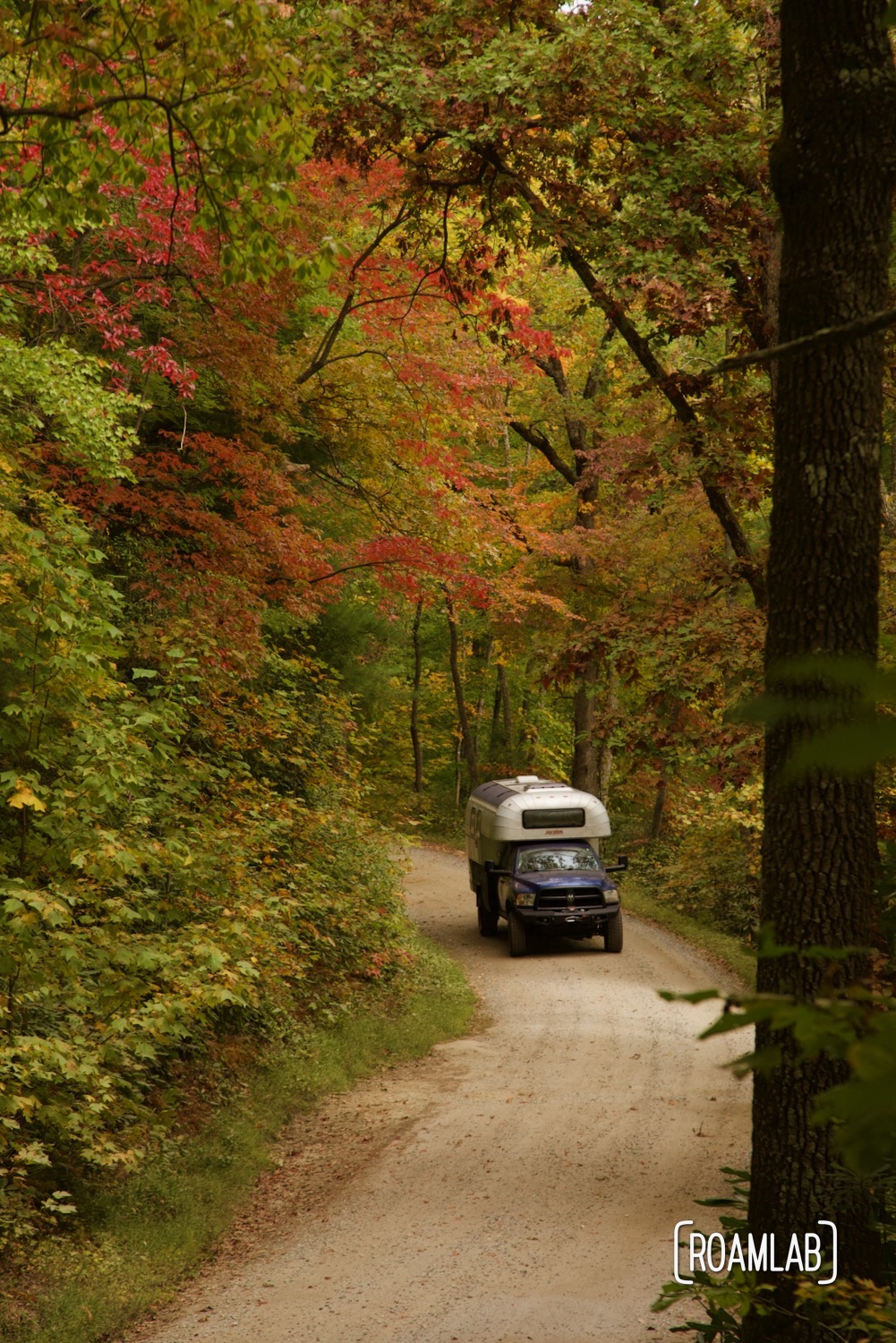 Bright fall colors surrounding a 1970 Avion C11 truck camper driving along the dirt Old North Carolina 105 in Linville Gorge Wilderness Area.