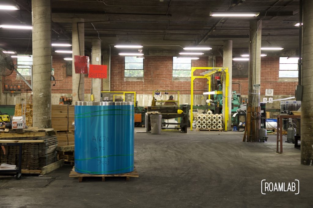 Roll of aluminum sheet in front of an industrial sheering machine to cut aluminum to size.