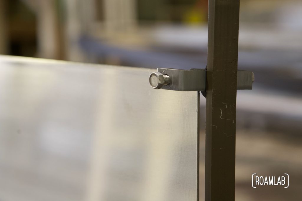 Closeup of an aluminum sheet secured to a frame with a screw clamp.