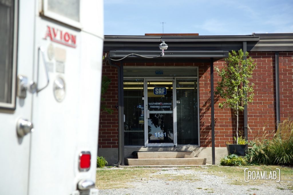 1970 Avion C11 truck camper parked outside a brick building with Southern Aluminum Finishing Co over the door on a clear blue sky day.