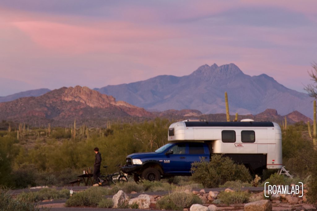 1970 Avion C11 truck camper parked in the desert with dry mountains in the distance illuminated pink and purple at sunset.