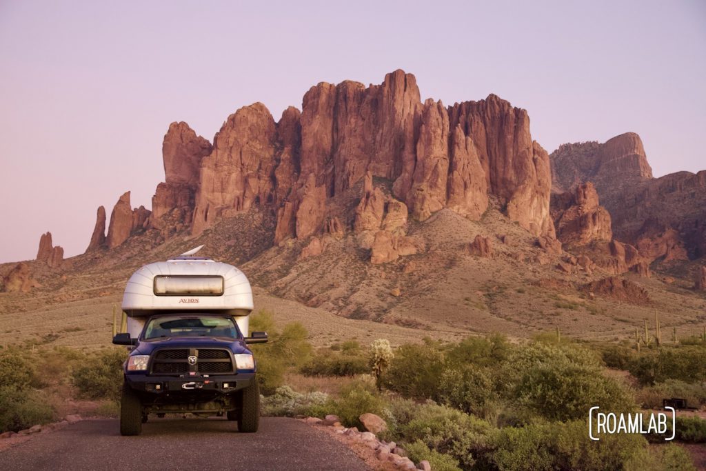 1970 Avion C11 truck camper parked in front of the Superstition Mountains in Lost Dutchman State Park at sunset.
