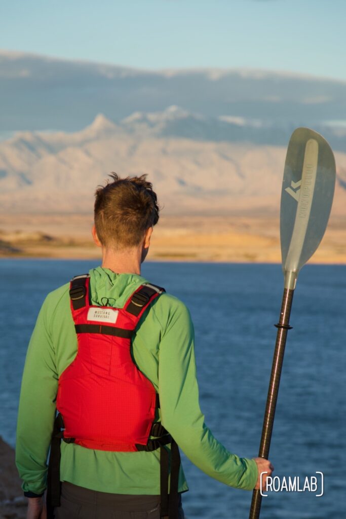 Man looking out over Lake Mead wearing a red life vest and holding a paddle.